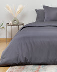 Gray bedding set on a bed with a side table and decorative items in a room.