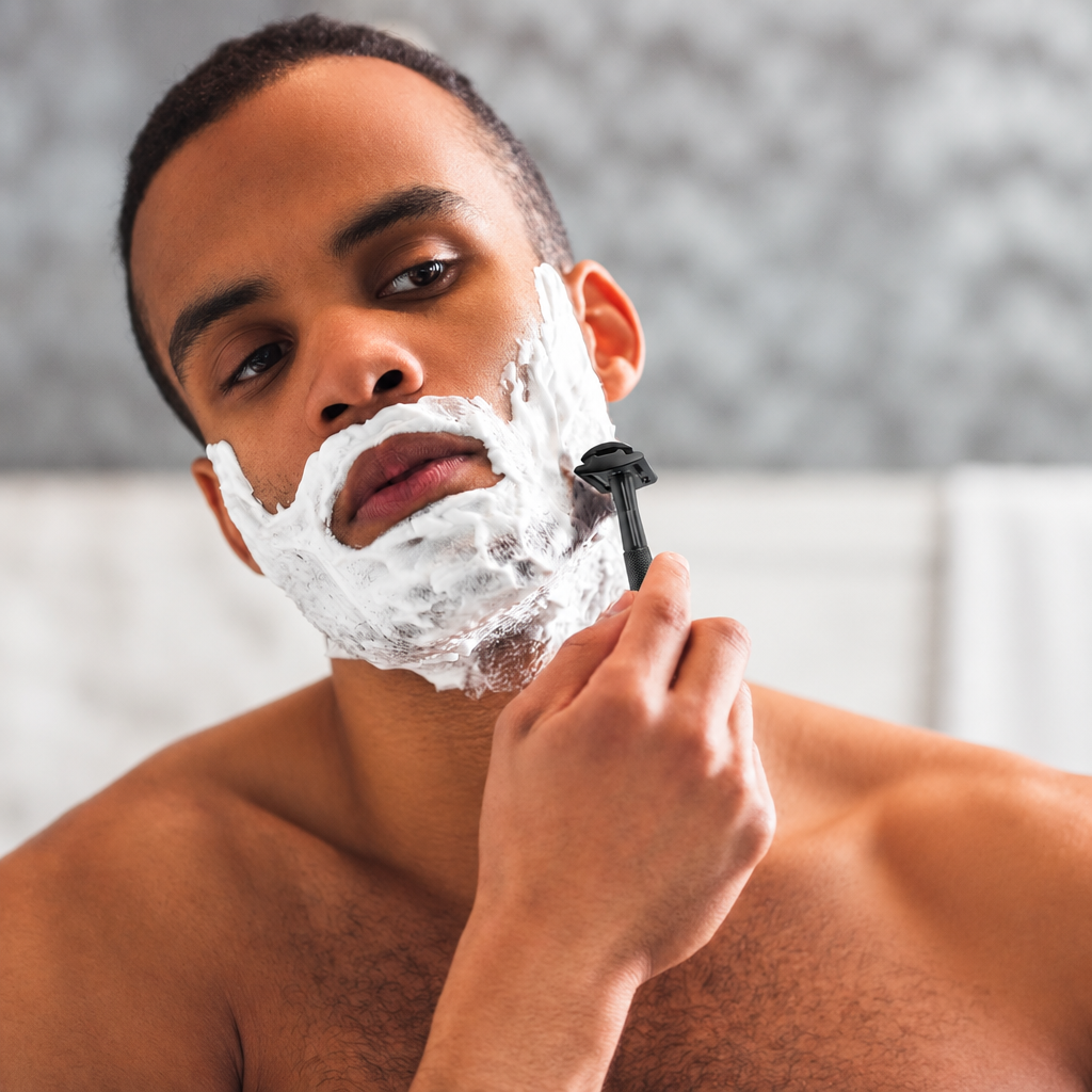 A close-up lifestyle shot of a man shaving with bambaw metal safety razor white shaving foam on his face, holding a black razor against his cheek.